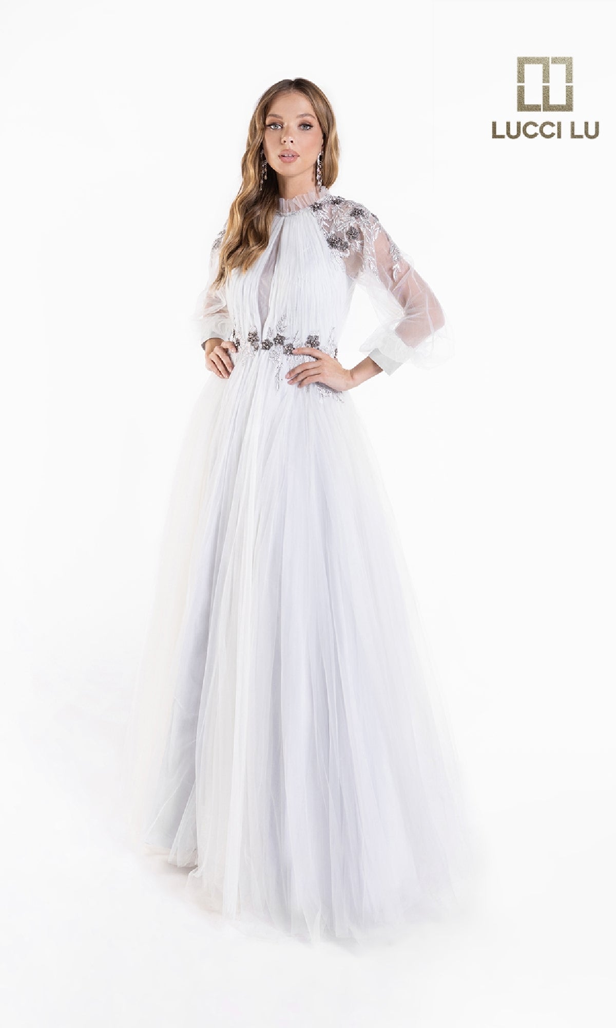 A woman models the Lucci Lu C8057 Long-Sleeve A-Line White Formal Dress, featuring sheer sleeves and floral embellishments, standing on a white background beside the Lucci Lu logo.